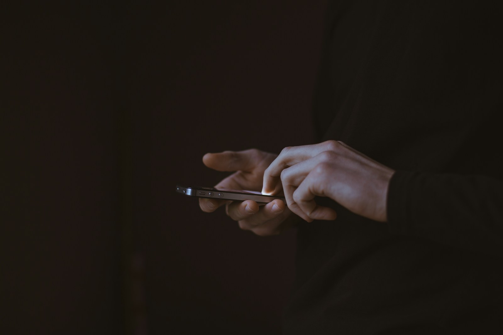 Dłoń trzymająca telefon na ciemnym tle