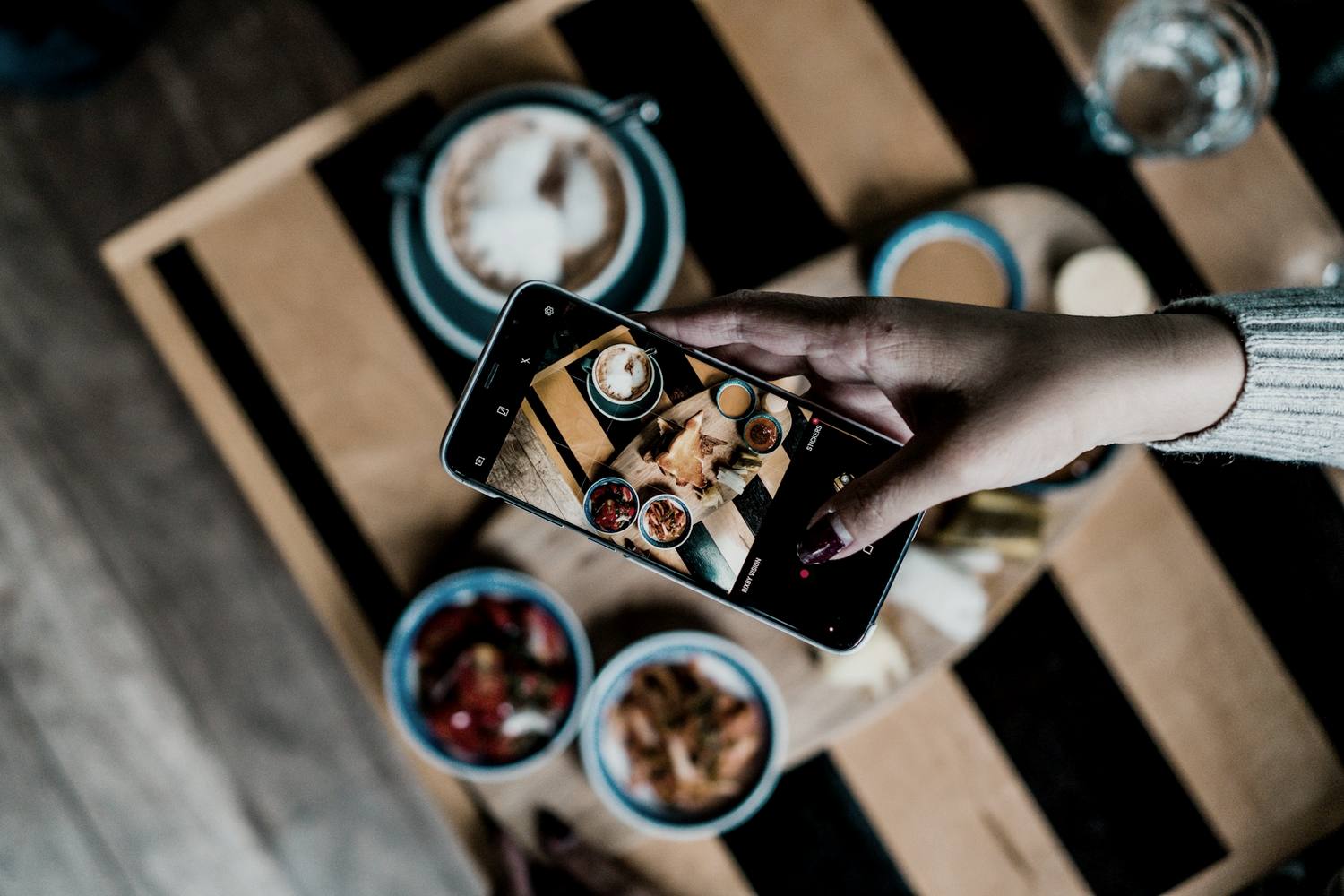 a hand photographing a table of food with a phone, the frame visible on screen